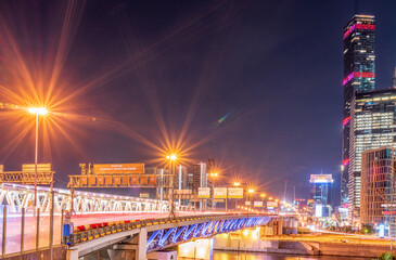 Fototapeta premium The scyscrapers of the Moscow City at night and the Dorogomilovsky bridge with illumination. Translation of text - street names: Krasnopresnenskaya, center, etc.