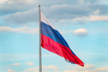 Russian tricolor flag waving in the wind against a blue sky.