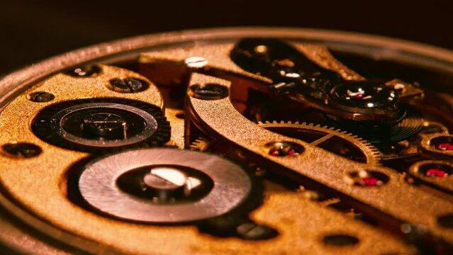Mechanism and gears of an old pocket watch. Macro close up shot. Camera moves left to orbit around the subject and light reflections move on the golden metal surfaces. Super slow motion.