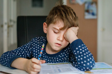 Hard-working sad school kid boy making homework. Upset tired child on home schooling, learning.