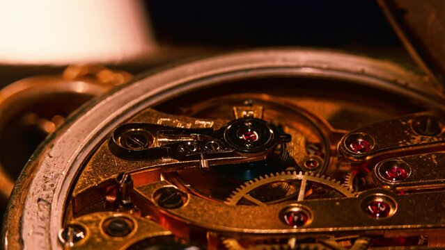 Mechanism and gears of an old pocket watch. Macro close up shot. Multiple layers of gears, camera moving left and lights in the background and reflections on the metal surfaces move.