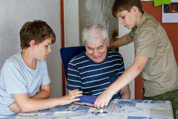 Obraz premium Two Preteen Boys Teaching Grandfather How to Use Internet Safely. Teenage Brothers, School Children with Digital Tablet Playing with Granddad, Senior Man at Home.
