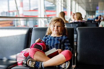 Little girl at the airport waiting for boarding at the big window. Cute kid holding passport..Looking forward to leaving for a family summer vacation