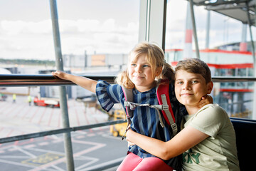 Little girl and school boy at the airport waiting for boarding at big window. Two kids stands at window against the backdrop of airplanes. Happy children, siblings leaving for family summer vacation