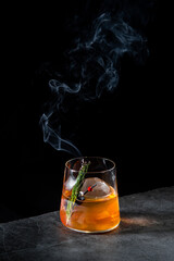 orange alcoholic cocktail with a sprig of pine needles and round ice, side view
