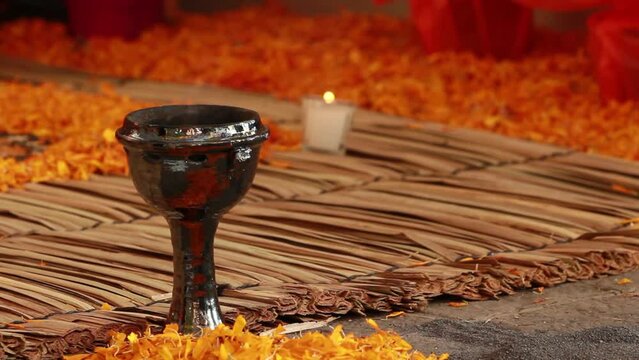 day of dead celebration, altar decorated with colorful yellow cempazuchitl yellow flower, candle, traditional handmade mexican carpet called petate, burning incense in a traditional copal made of clay