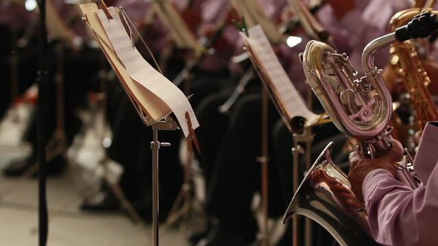 Music band of latino hispanic musicians playing wind instruments, baritone saxophone, reading their sheet music papers on a stand, classic music concert, people of hispanic brown skin