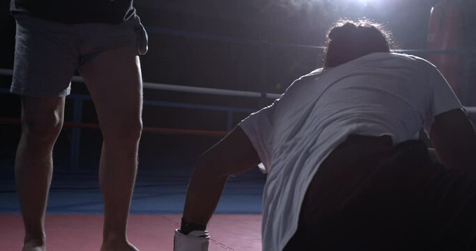 Fighter getting up from floor after being defeated by opponent, resilience theme of man raising himself up inside boxing ring
