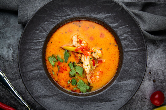spicy tom yum in a black plate with greens, top view