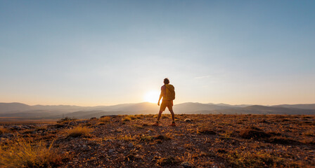 Fototapeta premium An active young man feels free. A confident man stands on a mountain against the background of a sunset. Experience freedom in the heart of nature.