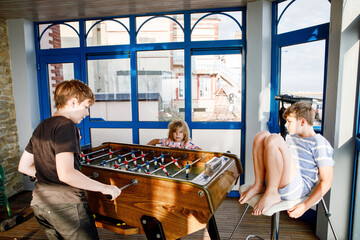 Little preschool girl and two kids school boys playing table soccer. Happy excited positive children having fun with family game with siblings or friends.
