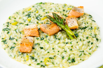rice porridge with artichoke, red fish and herbs in a white plate, side view