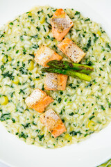 rice porridge with artichoke, red fish and herbs in a white plate, side view