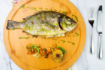 baked fish with lime and spices on a wooden tray on a marble background, top view
