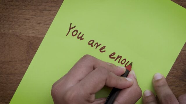 Affirmation of Self-Worth: Top-View of Hands Writing 'You Are Enough' on Green Paper