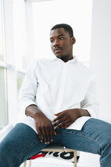 Fototapeta premium Young african man in white shirt and glasses posing near large window