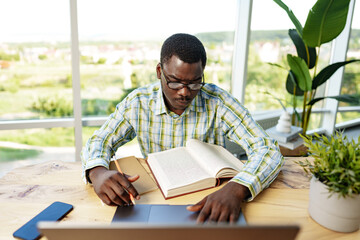 Serious concentrated african man studying or working with laptop indoors