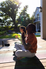 Happy diverse couple practicing yoga meditation sitting on deck in sunny garden, copy space
