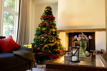 Decorated christmas tree by fireplace in sunny living room, copy space