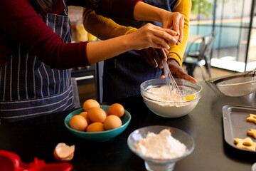 Midsection of diverse couple mixing dough for christmas cookies in kitchen