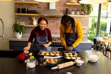 Fotobehang Happy diverse couple in aprons preparing christmas cookies in sunny kitchen © WavebreakMediaMicro