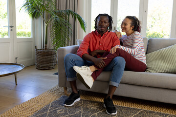 Obraz premium Happy diverse couple sitting on couch relaxing together in sunny living room, copy space