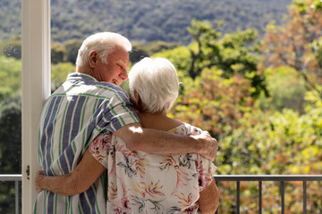 Back view of caucasian senior couple embracing and looking at each other on balcony on sunny day