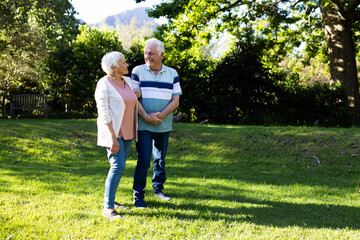 Fototapeta premium Happy caucasian senior couple walking, embracing and discussing in sunny garden, copy space