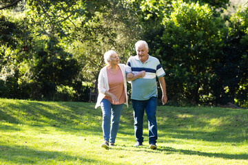 Happy caucasian senior couple walking, embracing and discussing in sunny garden, copy space