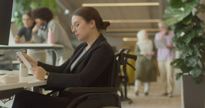 A businesswoman in a wheelchair is seen working on a laptop in a modern office, exemplifying a workplace that values inclusivity, accessibility, and professionalism.
