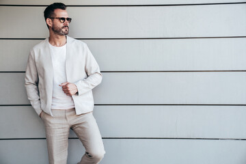 Portrait of handsome confident stylish hipster lambersexual model. Sexy modern man dressed in elegant suit. Fashion male posing in the street near urban wall. In sunglasses