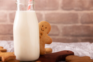 Homemade smiling gingerbread man cookie peeking out from behind a milk glass jar. These cookies are traditionally made in the holiday season for Christmas.