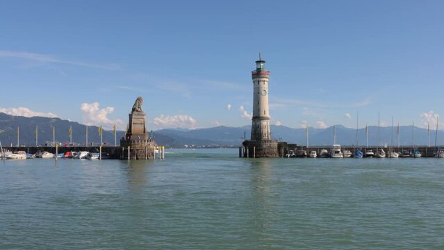 Tour boat enters, leaves old Lindau harbor past lighthouse, lion statue. Timelapse