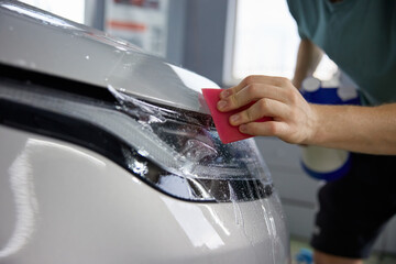 Closeup view on worker-detailer hands applying protective film on car headlight
