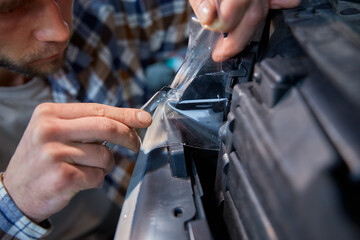 Cropped closeup view man working in garage applying protective film on headlamp
