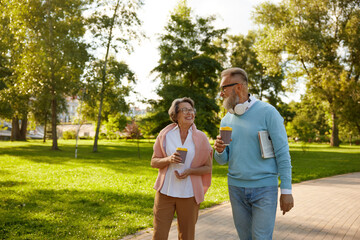 Happy fashioned elderly couple having coffee break walking in park - Powered by Adobe