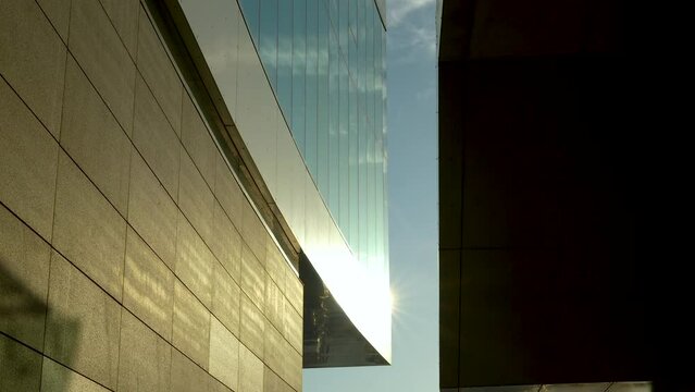 Sunlight shines between modern buildings with reflecting glass and stone walls.