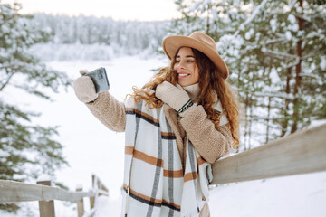 Happy woman in a hat and scarf with a phone in her hands taking a selfie in a snowy forest. Young...