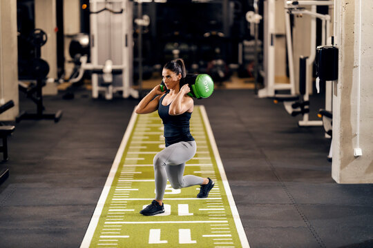 A motivated sportswoman is doing lunges while holding weights on her shoulders in a gym.