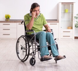 Young male invalid in wheel-chair suffering at home