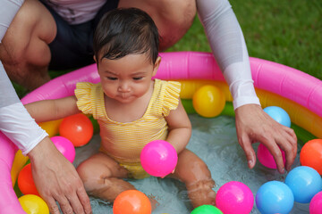 Fototapeta na wymiar happy father and infant baby girl playing water with colorful plastic balls in inflatable pool