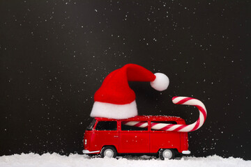 Toy car with Santa Claus hat on roof and candy cane on snowy dark night. Creative christmas background
