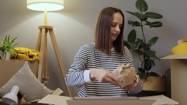 Calm woman sitting on floor packs up for relocation in new apartment surrounded by cardboard boxes full of stuff packing belongings in paper preparing for moving.