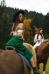 Foto op Canvas Young women ride horses in national Ukrainian dresses in the Carpathian mountains. Photo session with horses in the mountains. Ukrainian culture concept © Darius