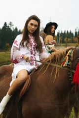 Foto op Canvas Young women ride horses in national Ukrainian dresses in the Carpathian mountains. Photo session with horses in the mountains. Ukrainian culture concept © Darius