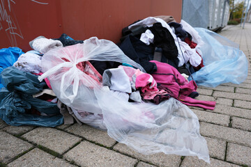 Umweltverschmutzung, aufgerissene Plastikbeutel mit alter Kleidung an einem Altkleidercontainer