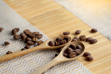 Fototapeta na wymiar Roasted coffee beans in wooden spoon and spread on woven bamboo placemat. It is a medium roast with medium intensity coffee flavor. Slightly sweet and sour, suitable for both hot and cold coffee.