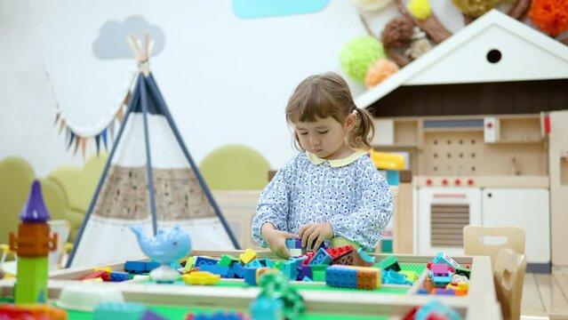 3-year-old girl construct wall from plastic building blocks or interlocking plastic bricks at playroom