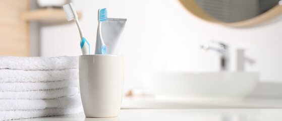 Plastic toothbrushes, toothpaste and towels on white table in bathroom, space for text. Banner...