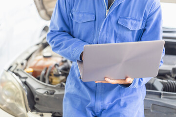 Auto mechanic working on laptop at mechanic shop, technician diagnosing car engine with a laptop with special program